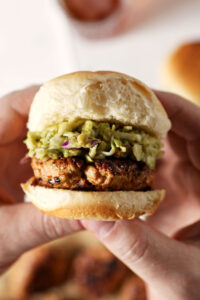 Hands hold a BBQ Chicken Slider with Avocado Slaw above a marble surface