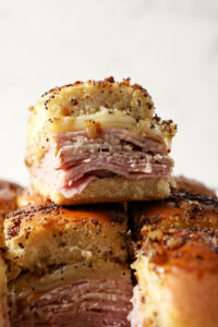 A stacked Baked Ham and Cheese Slider on top of other sliders in a sheet pan