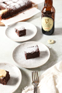 Three brownies on grey plates on a light green surface with a cream-colored linen